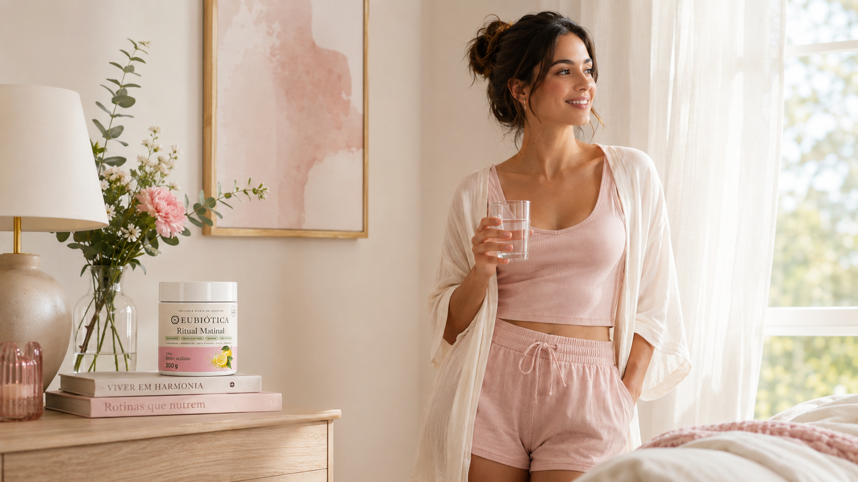 Mulher em roupa de dormir rosa com um copo de água ao lado do pote Ritual Matinal em um quarto claro